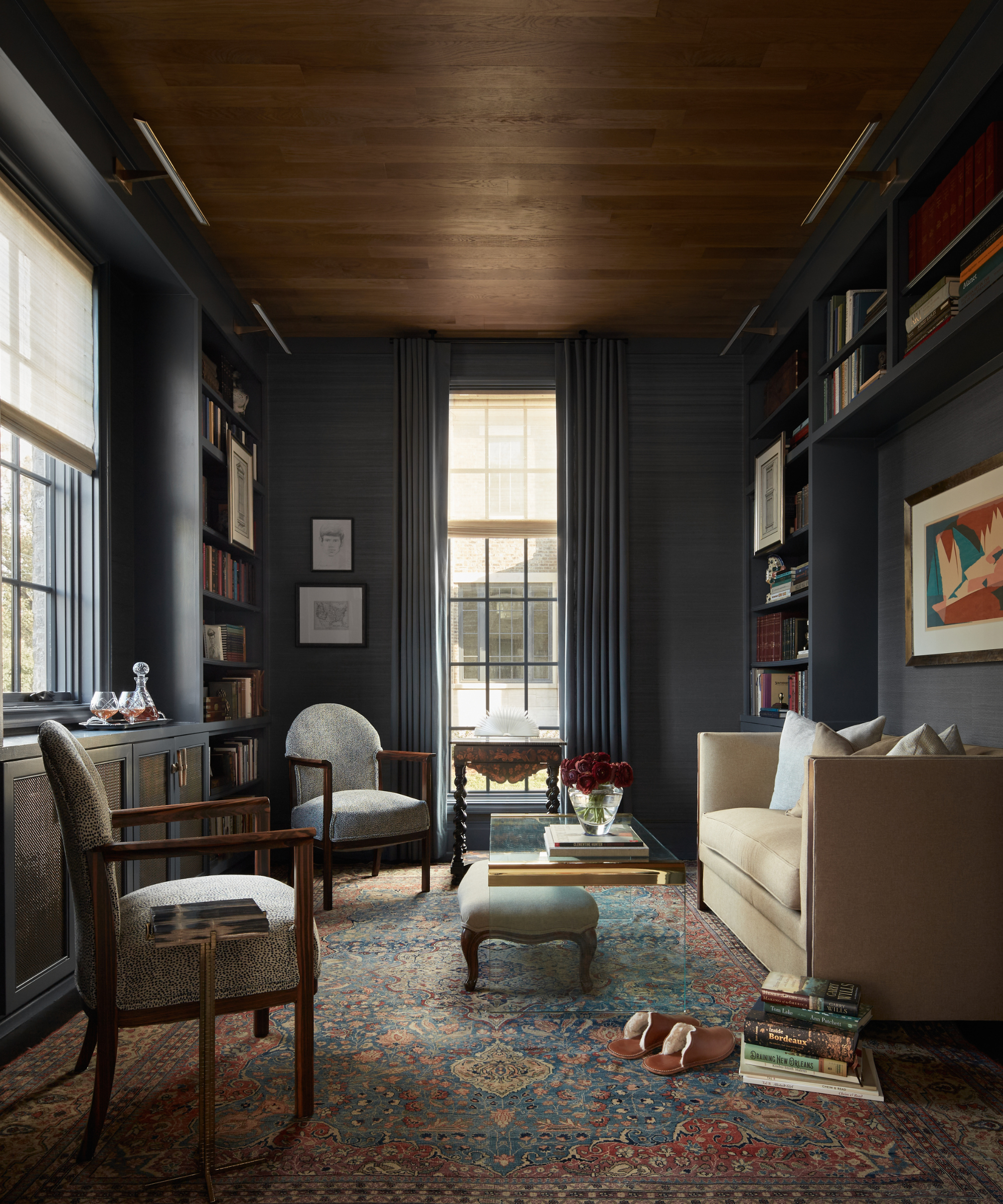 Eclectic study room featuring neutral furniture and a wood-paneled ceiling, anchored by a rich jewel-toned antique rug.
