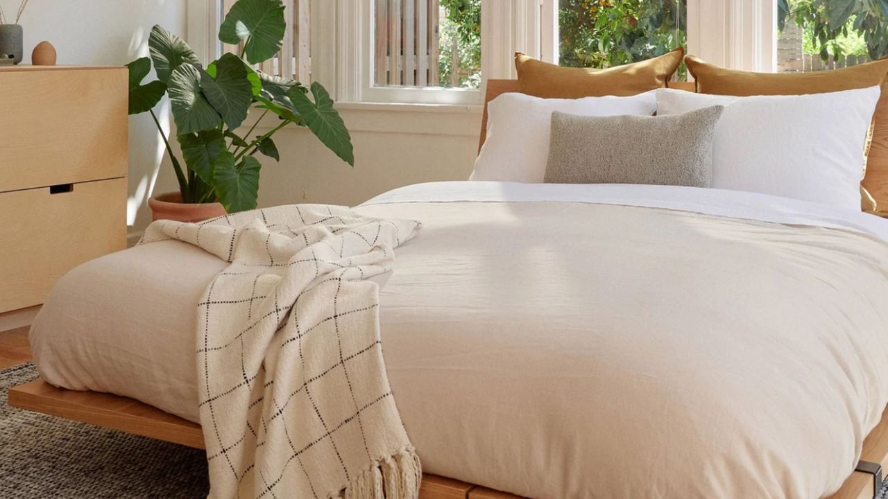 A modern wood bed frame in a neutral bedroom with plants