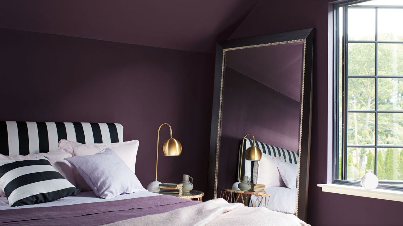 Deep purple bedroom with black and white striped headboard, purple bedding, large mirror and bedside table with gold lamp