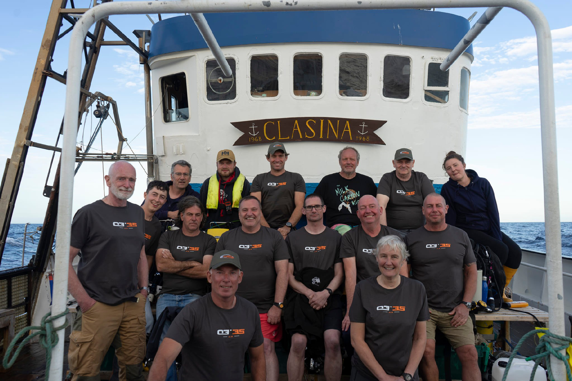 15 people pose for a group photo on the deck of a ship