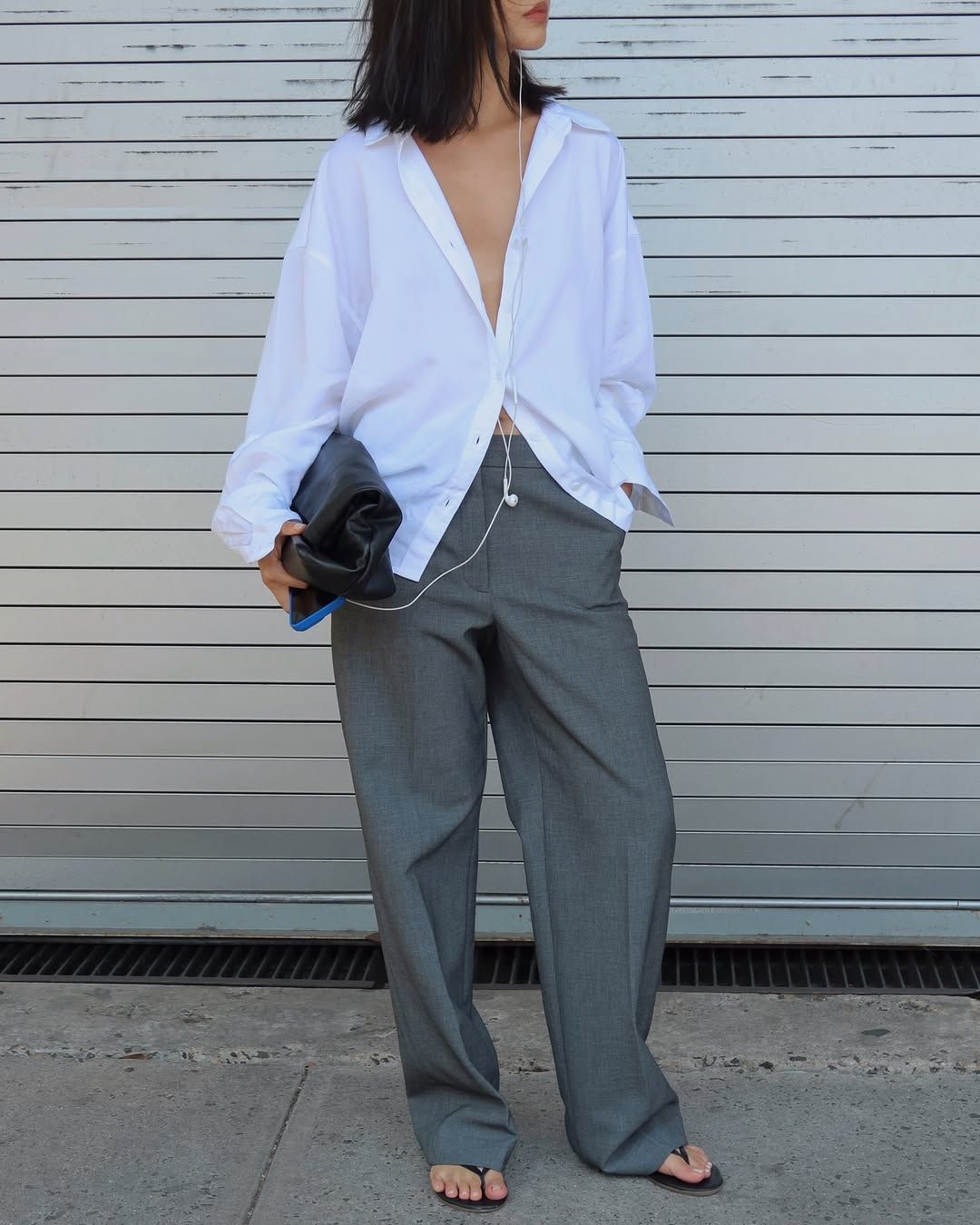 mimi wears a white shirt, grey trousers and flip flops