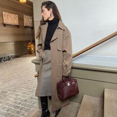 illrida wears camel coat black top pencil skirt and large wbrown ba