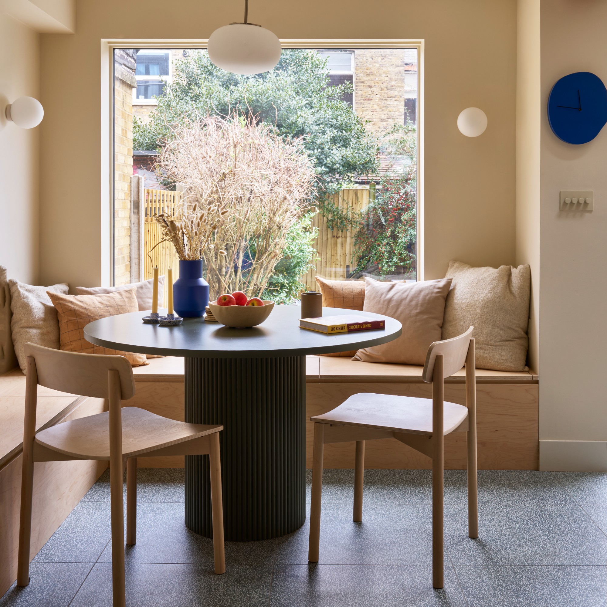 A kitchen dining nook with a round table with a reeded pillar leg and built-in wooden banquette seating