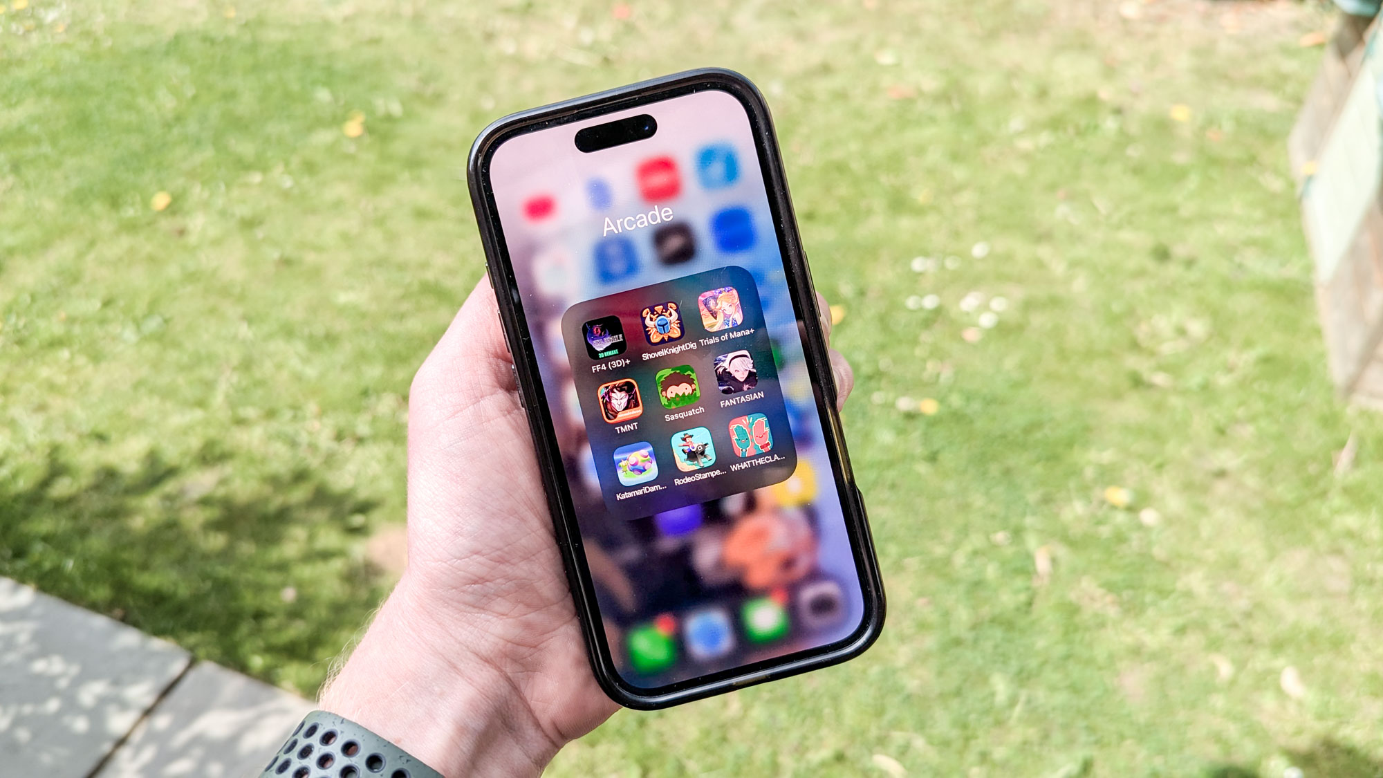 iPhone 16 in hand with grass in background showing Apple Arcade apps on display