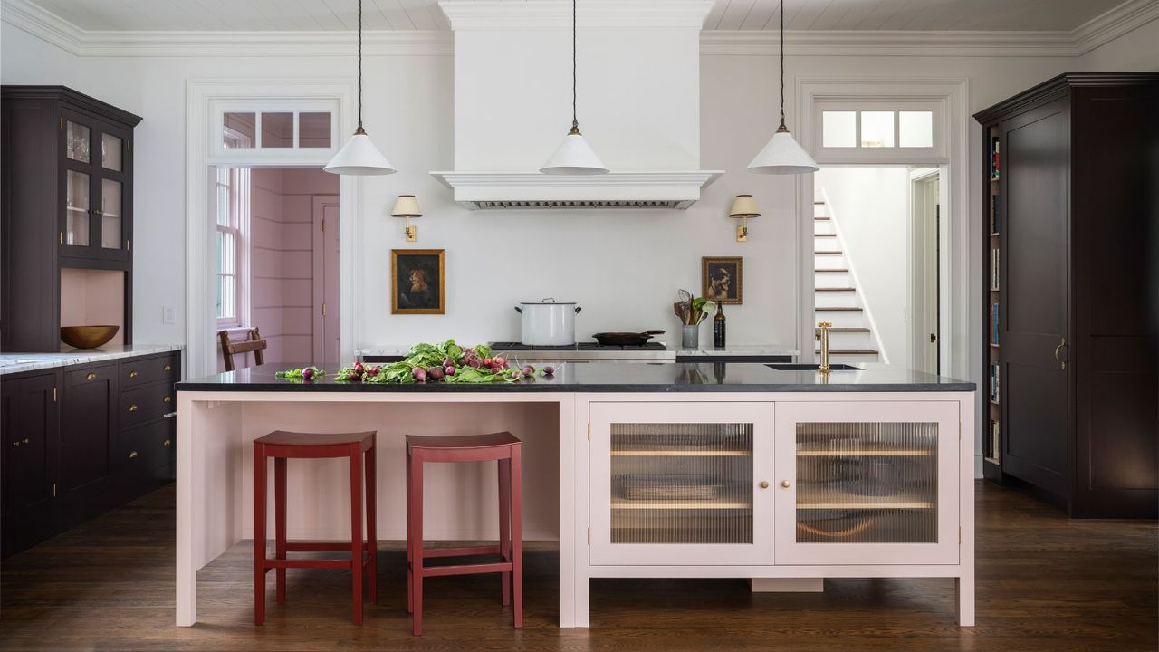 large kitchen with pink and dark blue cabinetry and red stools and white pendant lights and white walls