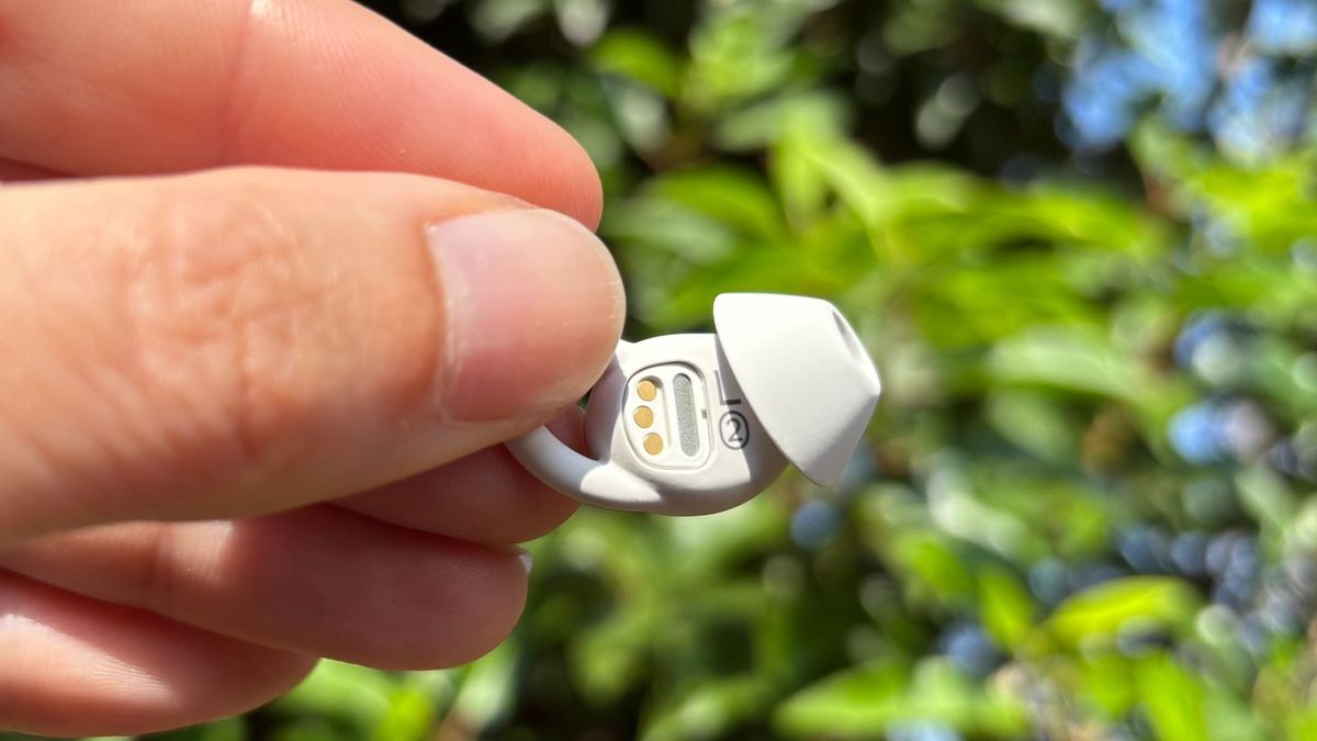 A hand holds the small white Ozlo Sleepbuds 2 against a backdrop of a green plant
