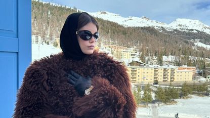 Kaia Gerber wearing a fuzzy brown coat with black leather gloves and black sunglasses
