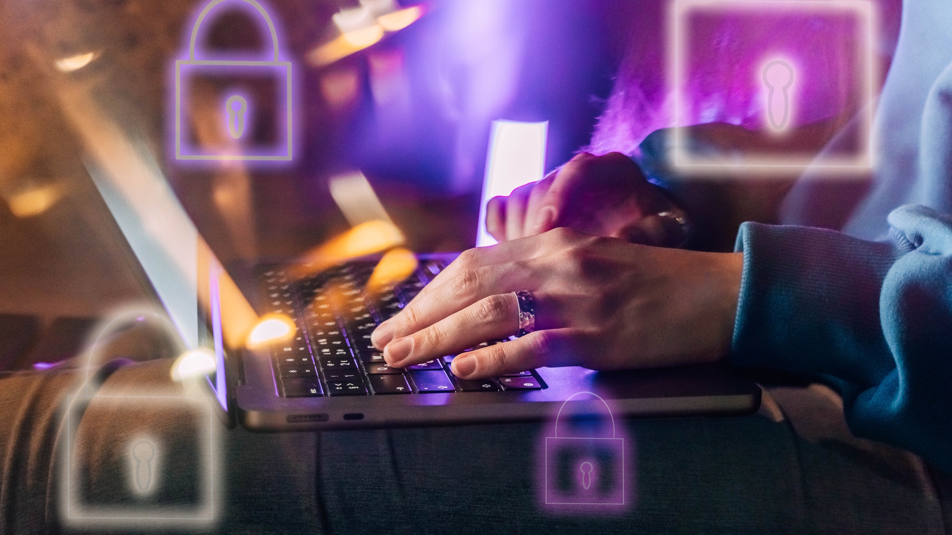 Female hands typing on a laptop in neon light. A lock as a symbol of cybersecurity on a foreground.
