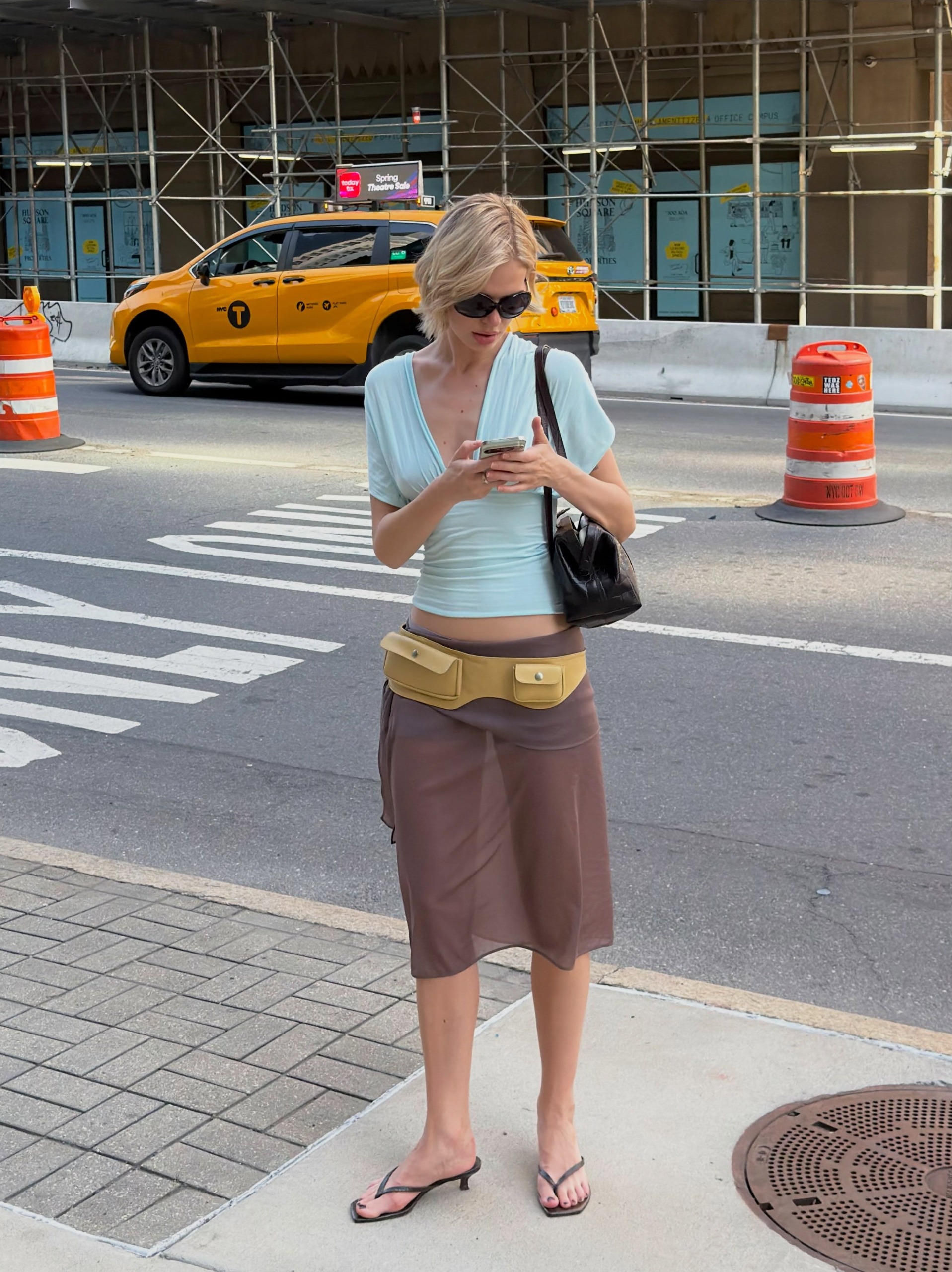 An image of @linda.sza wearing a sky blue top with a sheer chocolate brown skirt and a mustard-coloured coin belt.