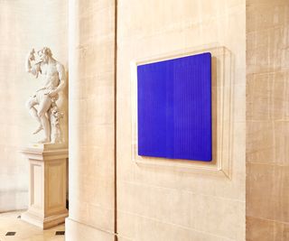 Glass framed blue square next to a stone statue