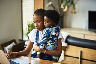 mum working from home on laptop while holding young child