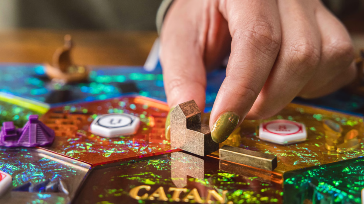 Sparkly Catan Hex tiles and metal buildings with a hand reaching down to move them 