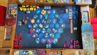 A top-down view of the Twilight Imperium board tiles, cards, and tokens on a wooden board gaming table