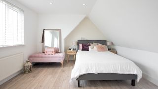 A plain white bedroom with sloped ceilings and a double bed