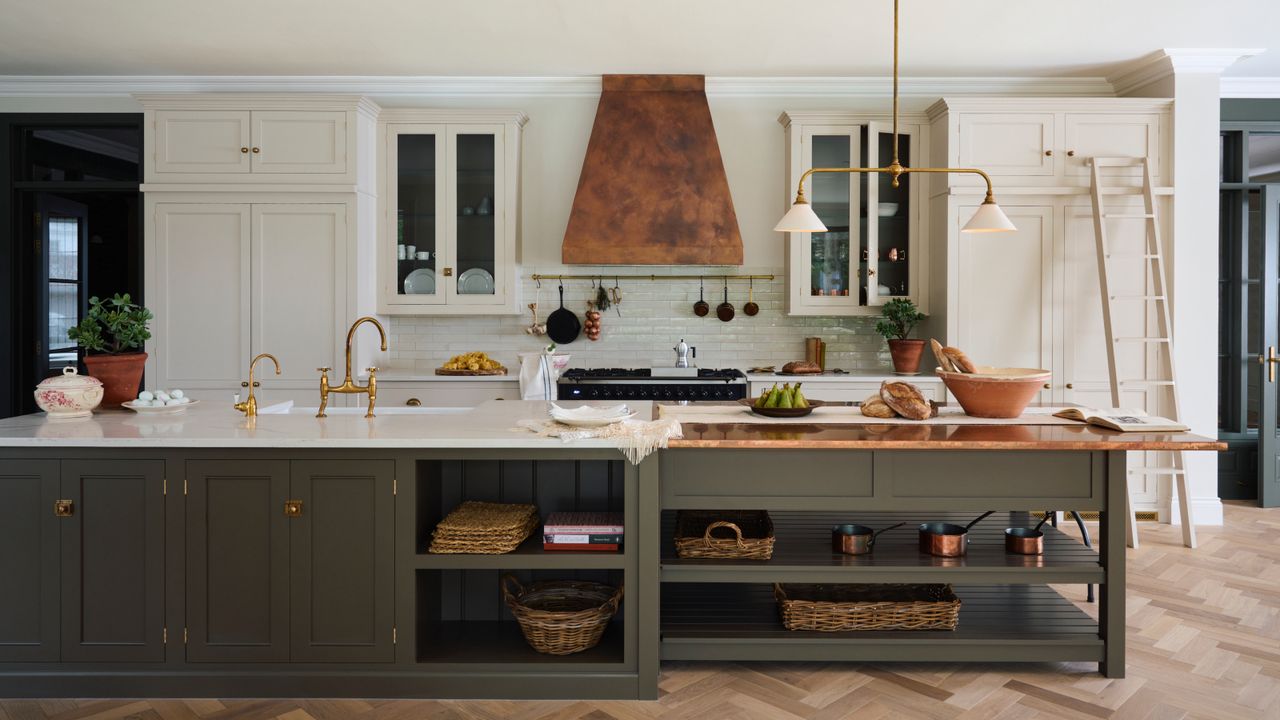 large white and sage green kitchen with parquet flooring, copper cooker hood, green island, white countertops, brass fixtures and fittings, glazed wall units