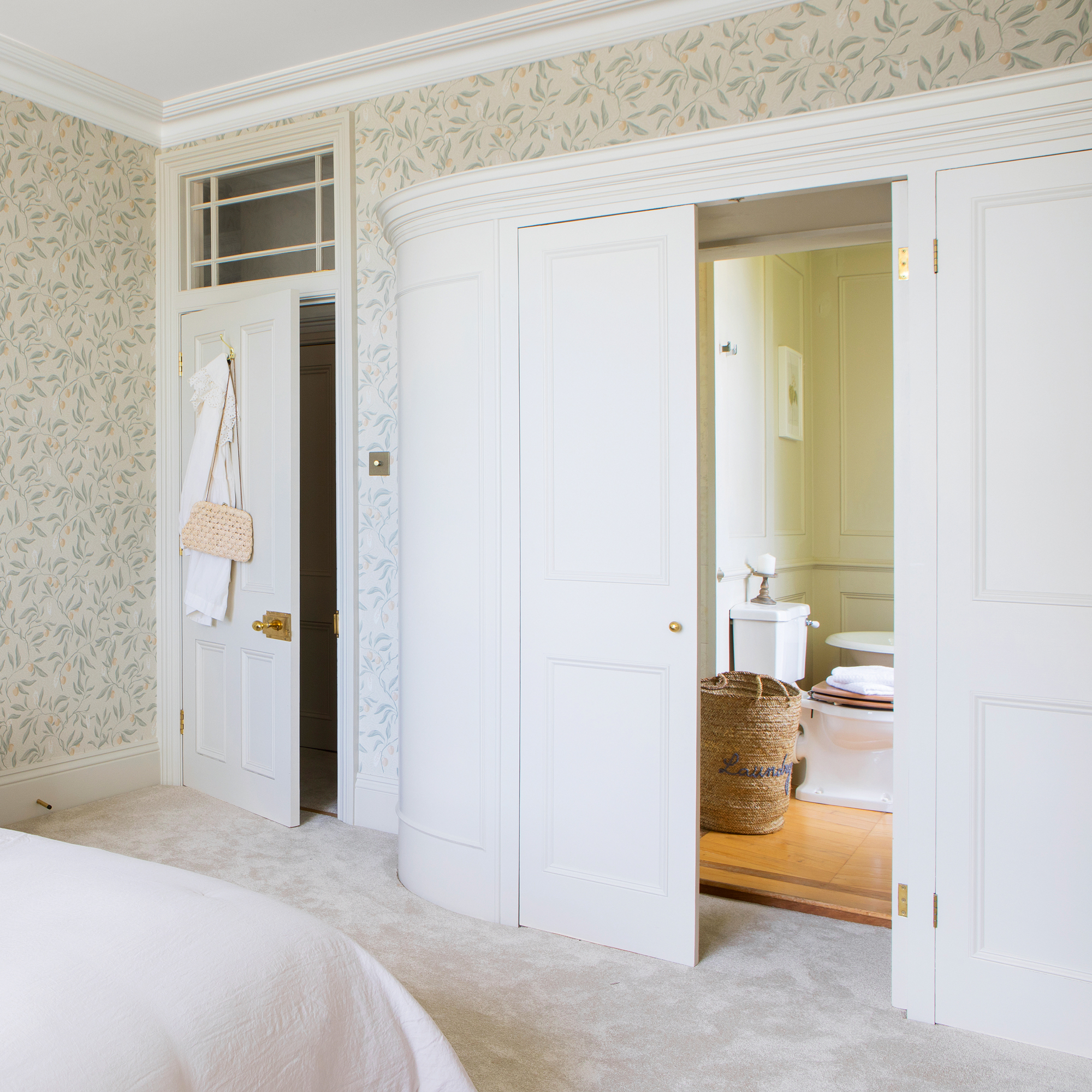 a bedroom leading into a bathroom through a door disguised as cupboards