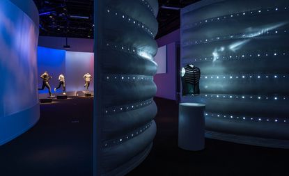 New Nike running and apparel innovations are showcased on mannequins. The space is dark with a spotlight on the clothes and sectioned with blue, curved divider walls.