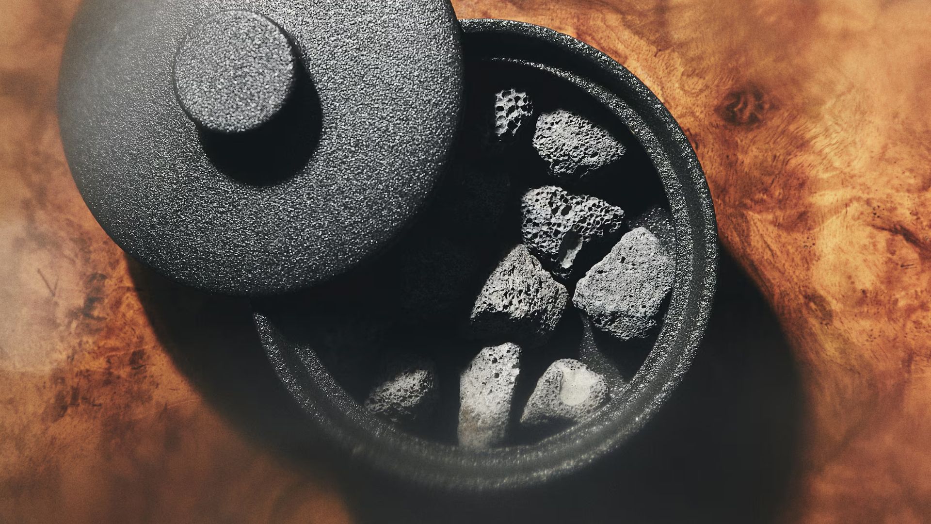 A close-up of a black vessel with a lava rock diffuser on a burl wood table