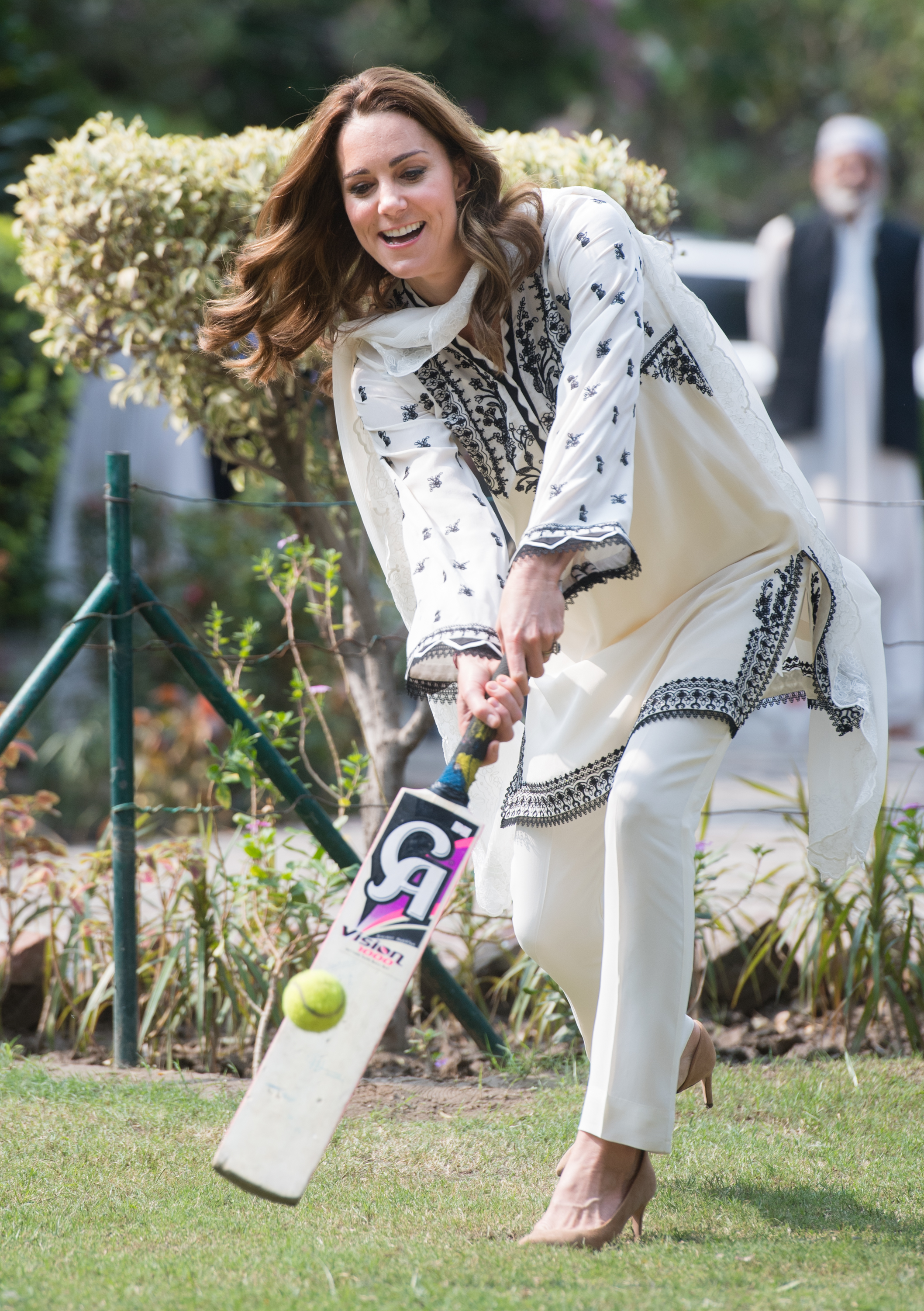 Kate Middleton wearing a white tunic and pants hitting a cricket ball