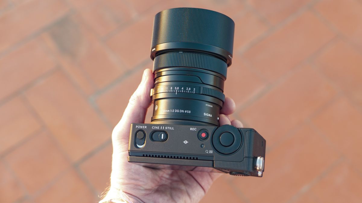 Sigma FP2 mirrorless camera with 50mm f/2 contemporary lenses attached, in users hand, theres a tiled floor background
