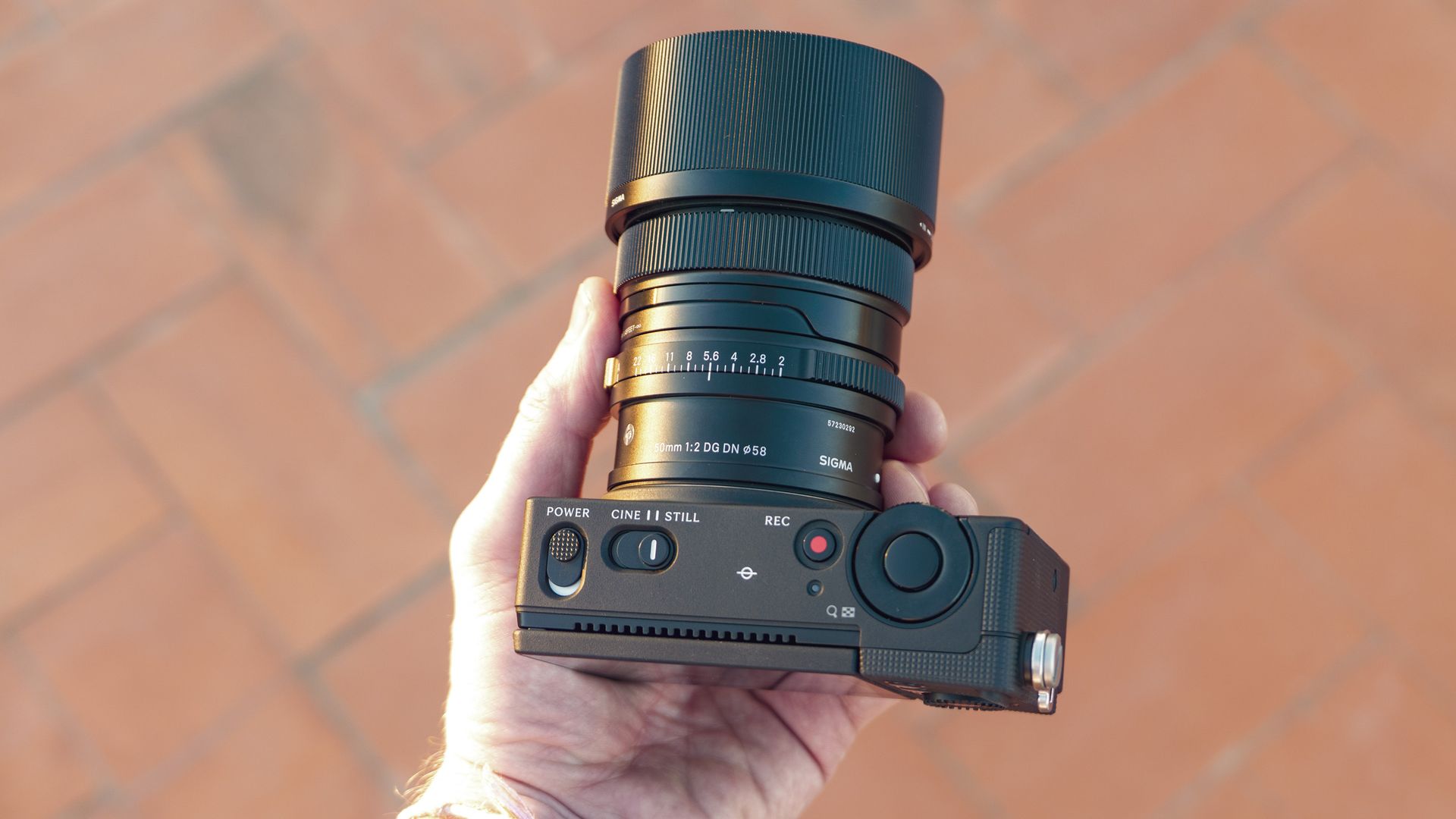Sigma FP2 mirrorless camera with 50mm f/2 contemporary lenses attached, in user's hand, there's a tiled floor background