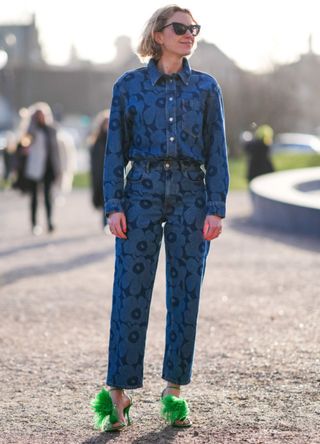 A guest wears sunglasses, a blue floral print shirt, matching denim jeans pants , green fluffy high heels shoes, outside Marimekko, during the Copenhagen Fashion Week AW24 on February 01, 2024 in Copenhagen, Denmark.