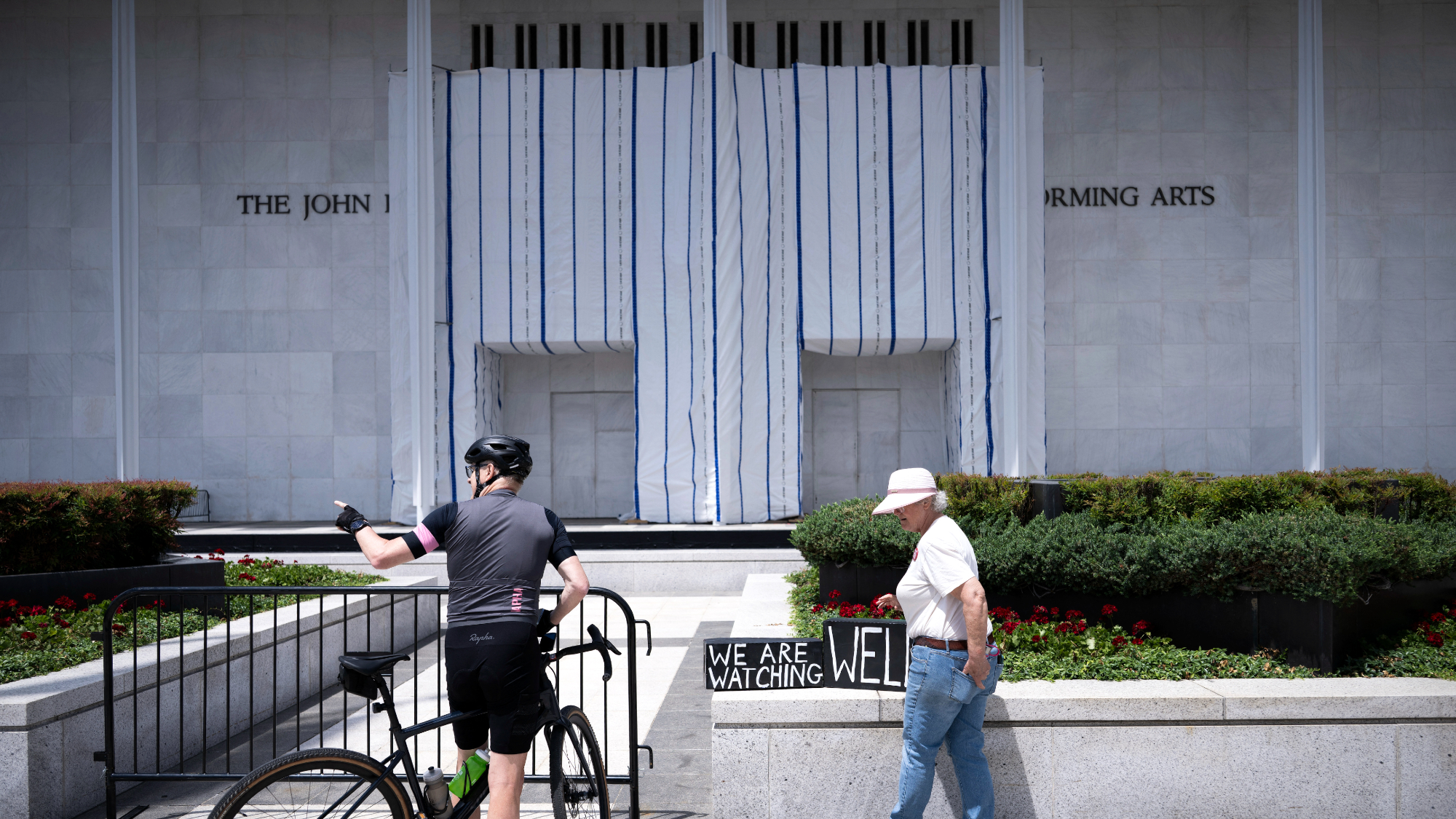People stand in front of a tarp covering signage on the facade of the Kennedy Center in Washington, D.C.