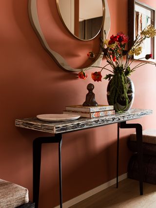 terracotta entryway with sculptural mirror, console, wooden floor, flowers