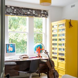 home office with computer on desk and guitar with yellow drawers and shutter window