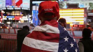 Supporter wearing "Trump" cap and American flag wrapped around his shoulders