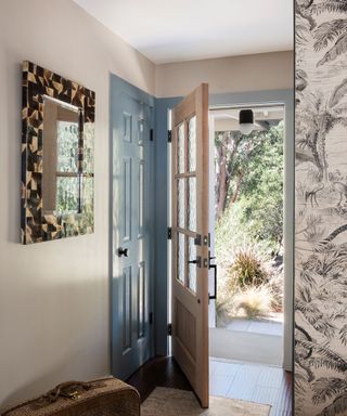 Entryway with tortoiseshell tile-framed rectangular mirror and blue door in narrow entryway