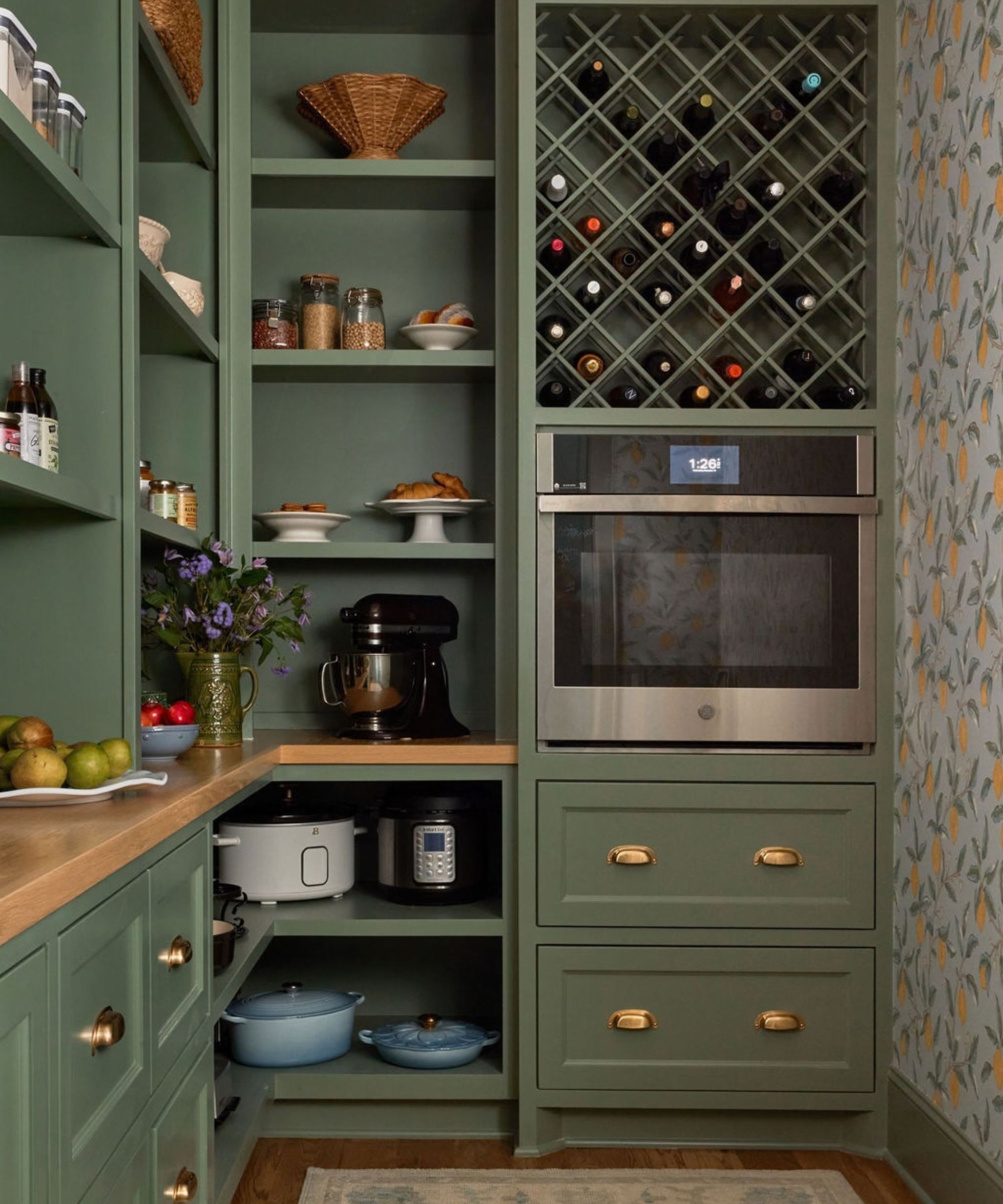 Olive green kitchen pantry featuring custom shelving, a lattice wine rack, a built-in wall oven, and small counter appliances