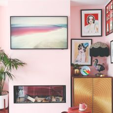 A pink-painted living room with alcove used for displaying art in a gallery wall style