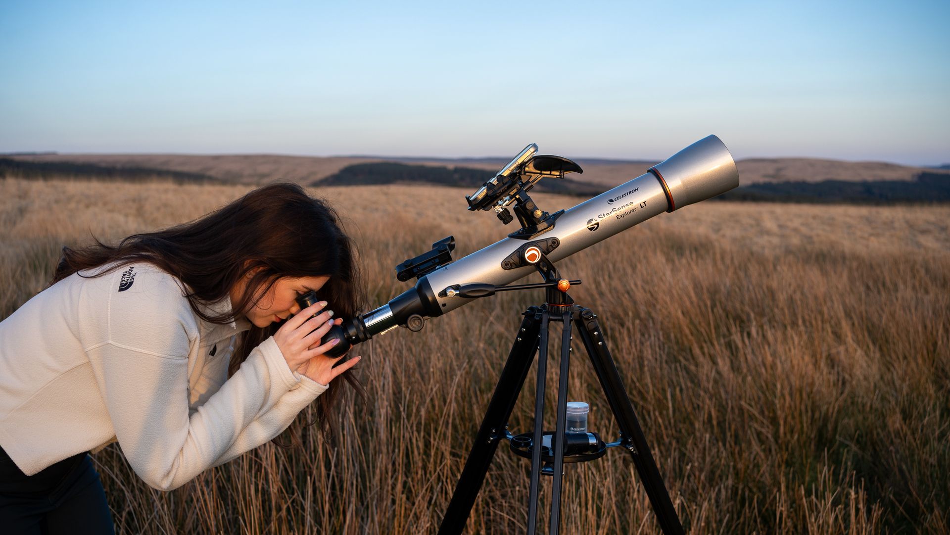 woman in a white top looking through the Celestron StarSense Explorer LT 70AZ