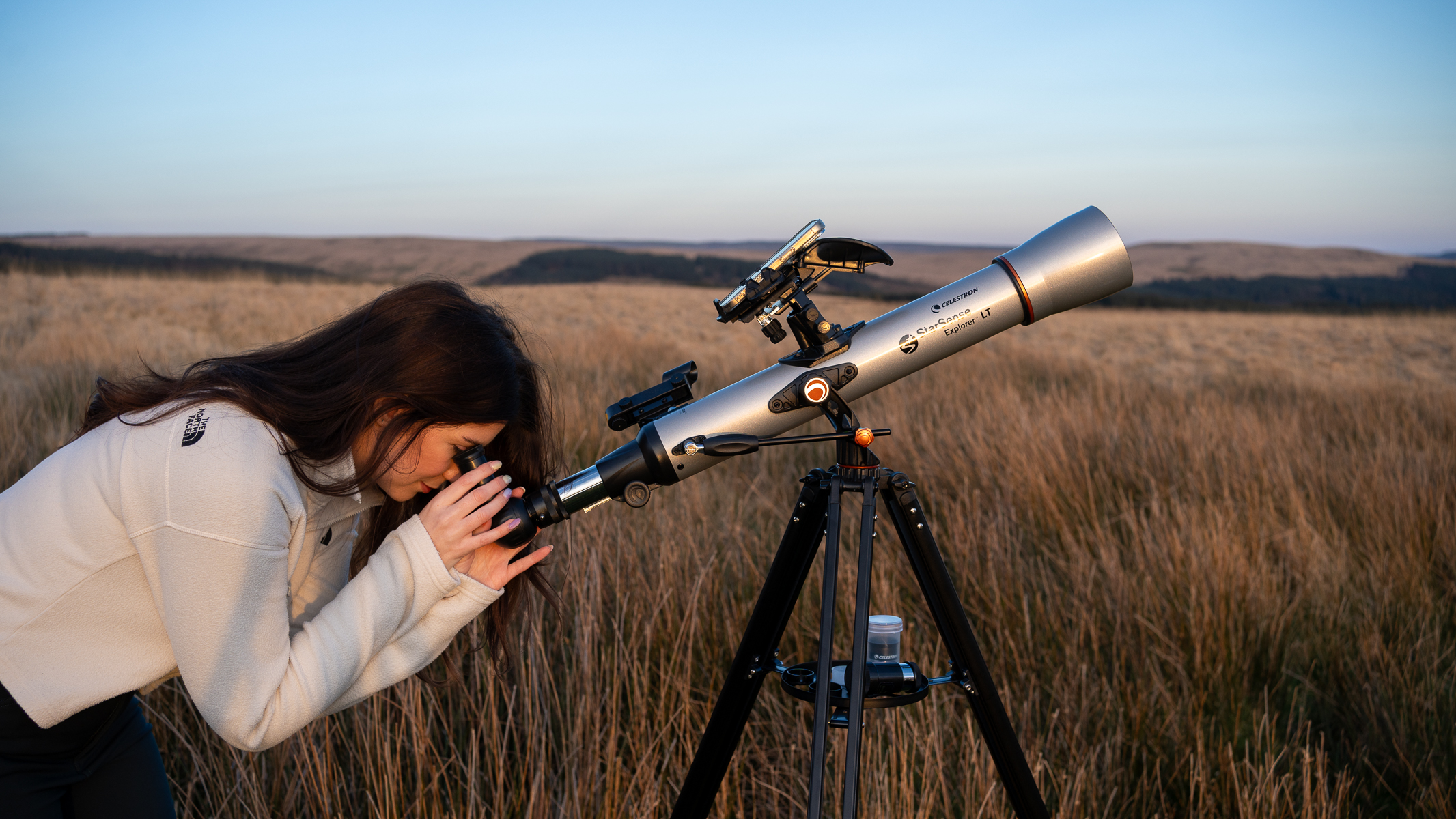 woman in a white top looking through the Celestron StarSense Explorer LT 70AZ