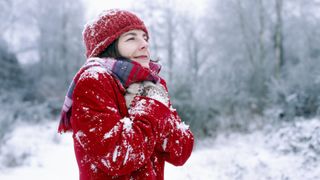A woman in a red coat shivers on a snowy walk