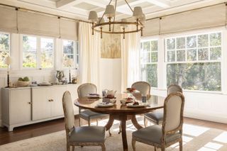 bright dining room with round table and windows on both sides with white sideboard and upholstered chairs