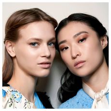 two models wearing white and blue shirts with glowing skin and bronze eyeshadow looks looking at the camera
