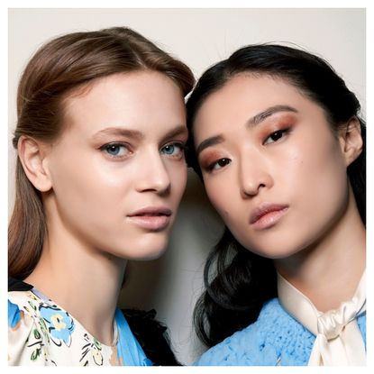 two models wearing white and blue shirts with glowing skin and bronze eyeshadow looks looking at the camera