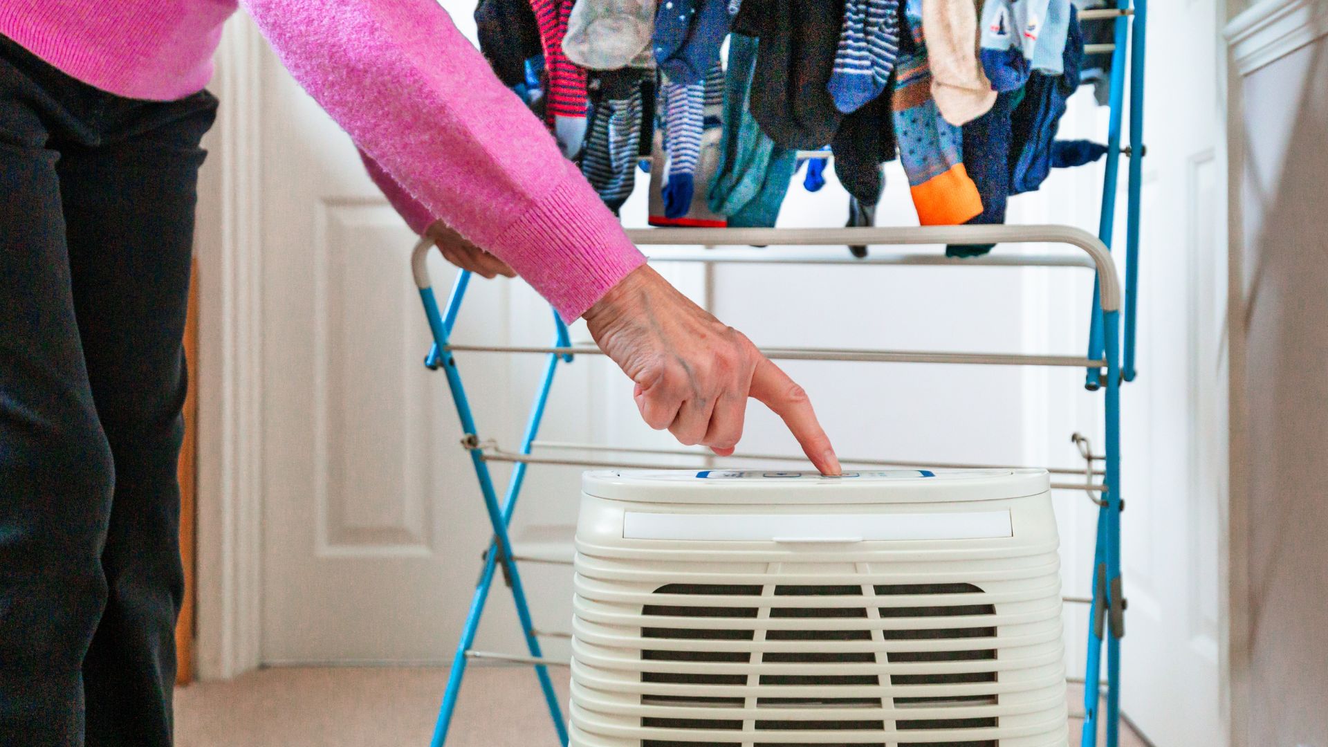 picture of woman turning on dehumidifier next to clothes airer