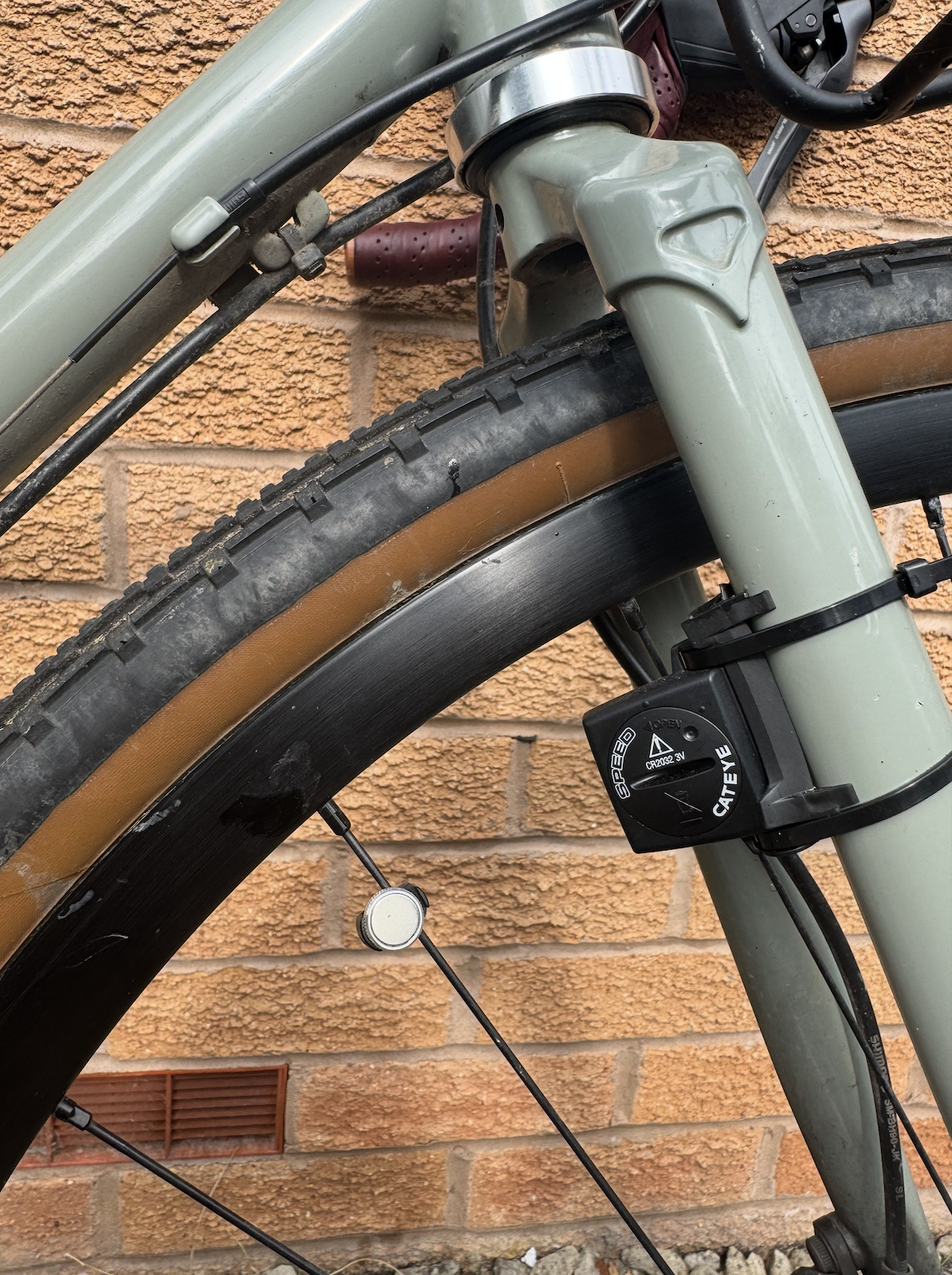 A teal coloured bike fork with a small black sensor zip tied to it. There is a small circular sensor on the spoke. 
