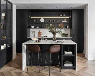 Kitchen with black units and island and white counters, and wood floor and white walls