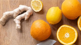 Whole oranges and a ginger stem sitting on chopping board