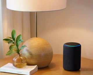 Amazon Echo 3rd Generation on a table near a lamp and book