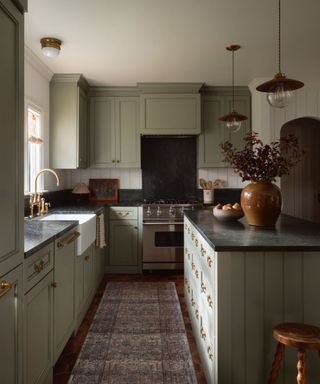 soft green small kitchen with dark marble countertops, a small island decorated with vintage pieces and a runner rug