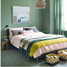 bedroom with green walls and carpets, abstract painting, double bed with pink duvet and storage baskets