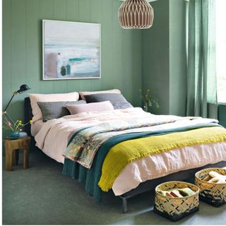 bedroom with green walls and carpets, abstract painting, double bed with pink duvet and storage baskets
