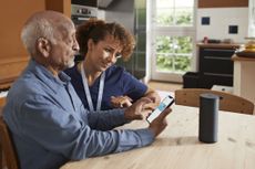 Female nurse teaching senior man to book online appointment through smart phone at table