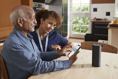 Female nurse teaching senior man to book online appointment through smart phone at table