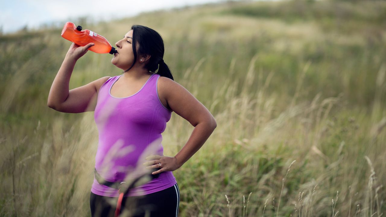 Woman drinks from water bottle as she exercises outdoors